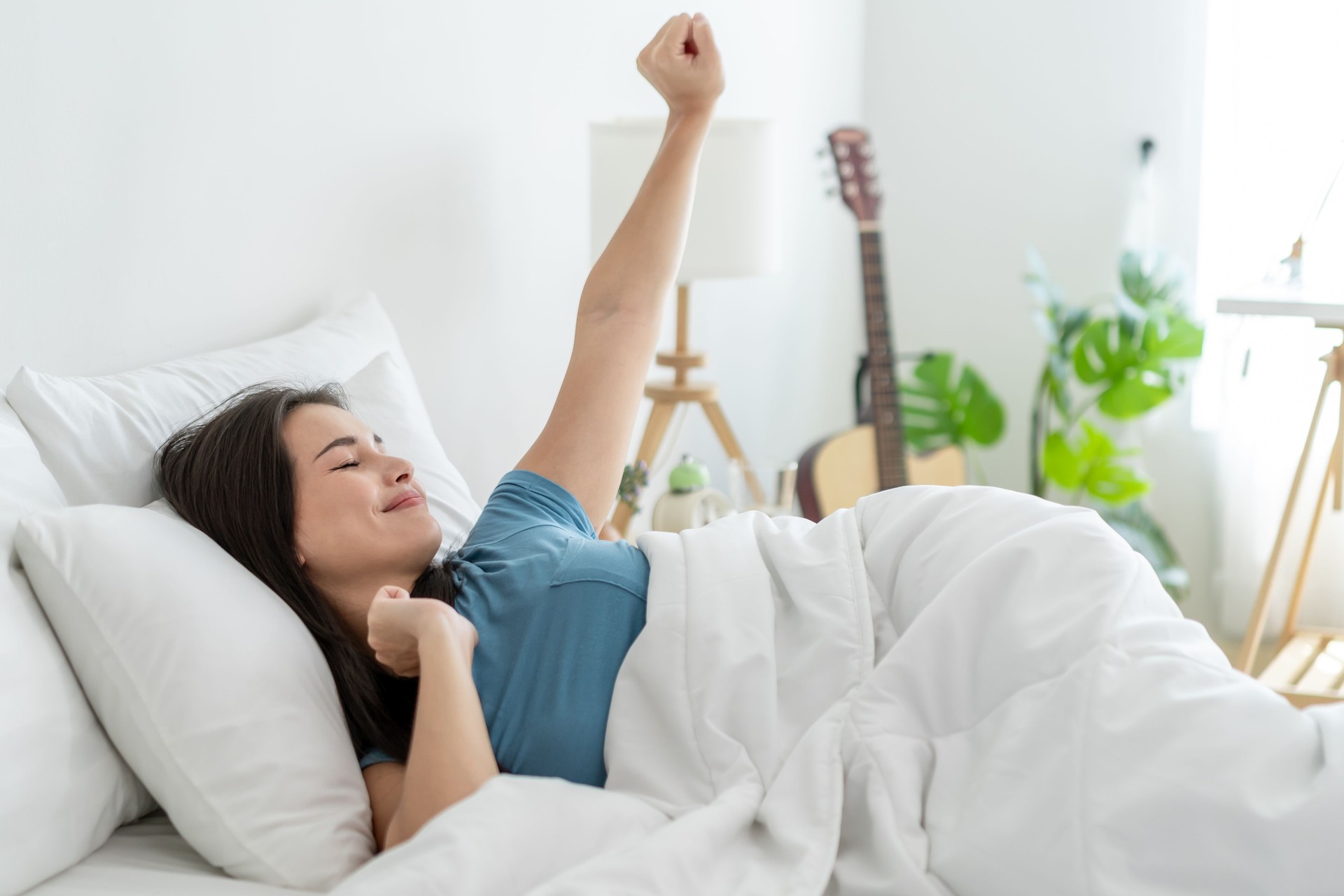 Asian young beautiful woman getting up from sleep on bed in the morning. Attractive girl in pajamas feeling happy and relax, wake up and stretching body during holiday weekend in bedroom at home.