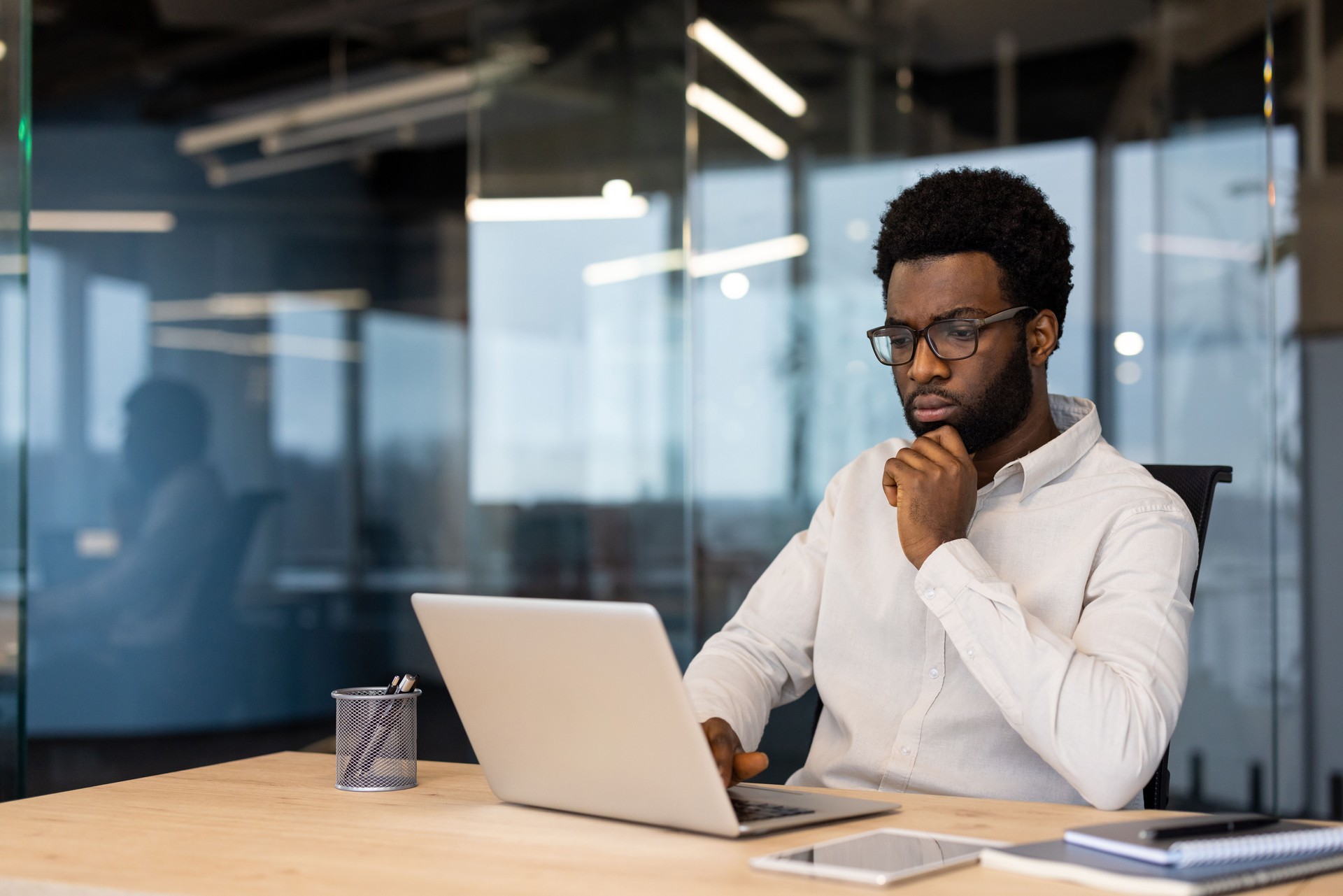 African American businessman working thoughtfully at laptop in modern office setting showcasing concentration and analysis in corporate environment with technology and professional attire
